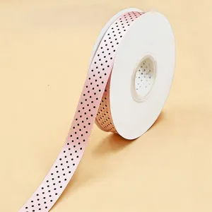 Primo piano di nastro in raso rosa con pois neri arrotolato su rocchetto per la decorazione.