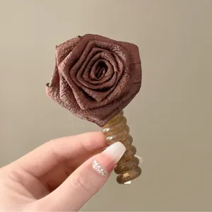 Primo piano dettaglio fiore di rosa in tessuto marrone con elastico per capelli elegante accessorio.