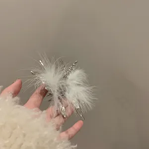 Close-up detail of silver liquid butterfly hair claw decorated with fluffy white feathers.