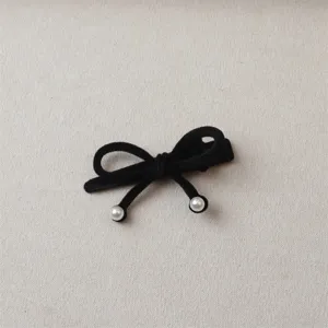 Close-up detail of black velvet bow hair clip with pearl embellishments, elegant style.