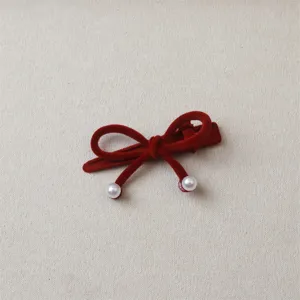 Close-up shot of the red velvet bow hair clip, showing soft texture and delicate pearl details.