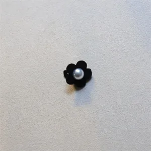 Close-up detail of a chic black velvet flower hair clip featuring a glossy center pearl accent.