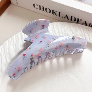 Nahaufnahme einer hellblauen Haarklammer mit Rosenmuster auf einem weißen strukturierten Teller