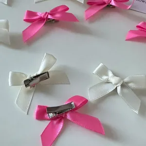 Mini bow hair clip detail view showing cute satin ribbons and metal alligator clips for sweet styling.