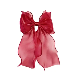 Detailed view of a large red organza hair bow with flowing ribbons, sheer fabric accessory.