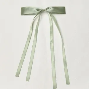 Detailed shot of a sage green satin ribbon bow hair clip, featuring elegant double trailing ribbons.