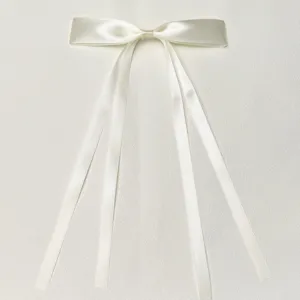 White satin ribbon bow hair clip detail, showing smooth polyester fabric and long double streamers.
