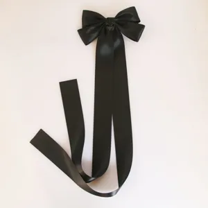 Black satin bow hair clip detail, featuring an oversized design with long flowing ribbons.