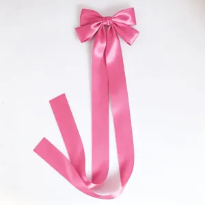 Pink satin bow detail with long flowing ribbon, sweet style hair accessory close up.