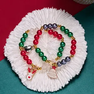 Détail de bracelets de Noël en perles avec breloques renne et sapin sur assiette corail blanc.