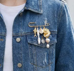 Detailed view of an ocean-themed safety pin brooch with shells and pearls on denim jacket