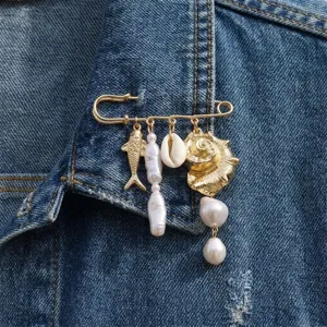Detailed view of an ocean-themed safety pin brooch with pearls and charms on denim