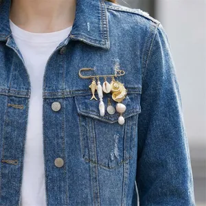 Close-up of a gold seashell and pearl charm brooch pinned to a blue denim jacket.