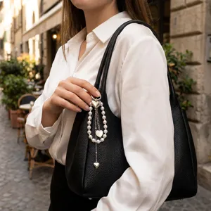 Elegante ciondolo per borsa in perle con cuore d'argento su una borsa in pelle nera