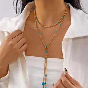 Close-up detail of a multi-layer gold Y-necklace featuring turquoise beads on a female model