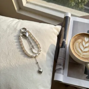 Ciondolo borsa cuore con perle finte e catene d'argento su un cuscino bianco