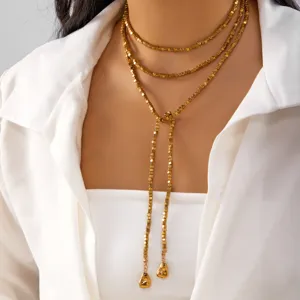 Detail of a multi-layer gold cube bead Y-necklace with long tassels on a white shirt