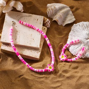 Detailansicht eines rosa-weißen Tonperlen-Schmucksets mit Plumeria-Blumen auf tropischem Sand