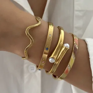 Detailopname van een set van vier vintage goudkleurige roestvrijstalen armbanden op een pols.