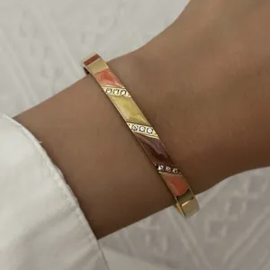 Close-up van een gouden roestvrijstalen armband met kleurrijk emaille en kleine kristallen