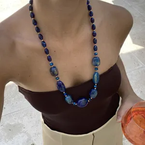 Collana di perle in resina blu irregolare indossata da modella con top marrone