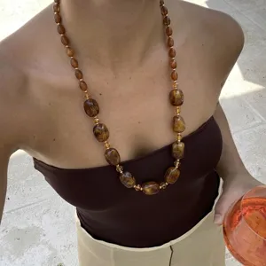 Primo piano di una collana di perle di resina marrone con motivo tartarugato su modella