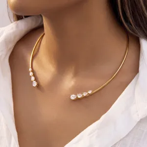 Gros plan d'un collier ras de cou en acier doré orné de zircons étincelants en goutte.