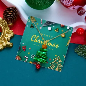 Festliche Weihnachtsbaum-Halskette mit roter Perle auf dekorativer Karte.
