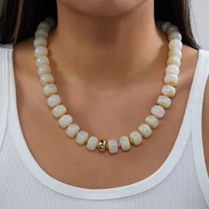 Gros plan d'un collier de perles crème fait main avec accent doré porté par un mannequin