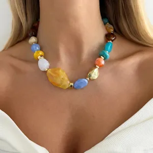 Close-up view of a colorful irregular resin bead necklace worn by a female model in white