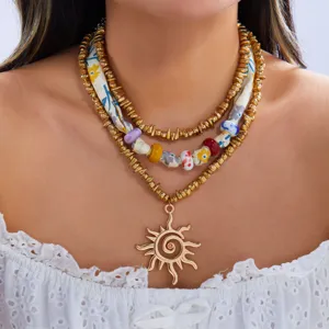 Detalle de un conjunto de collares bohemios con colgante de sol, pañuelo floral y cuentas CCB doradas