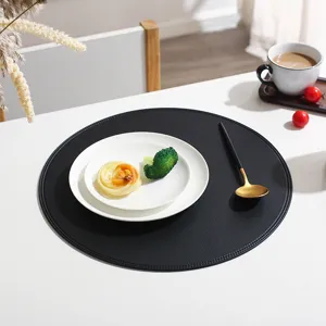 Closeup of a sleek black round leather placemat on a dining table with chic tableware.