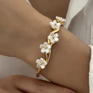 Detailansicht eines eleganten goldfarbenen Armbands mit weißen Blumen am Handgelenk.