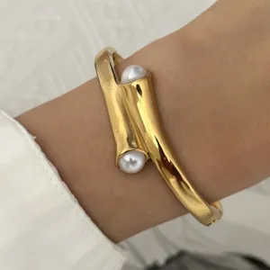 Close-up van een elegante gedraaide gouden armband met twee parelaccenten om een pols.