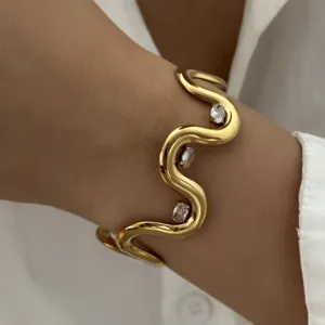 Detailansicht eines eleganten goldenen Wellenarmbands mit ovalen Edelsteinen an einem Handgelenk