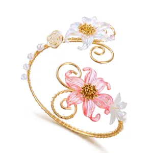 Dettaglio ravvicinato di un bracciale da braccio floreale in filo dorato e petali rosa.