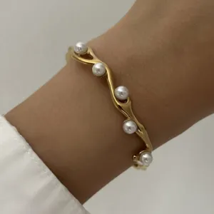 Detail van een gouden gedraaide armband met elegante witte parels om de pols gedragen