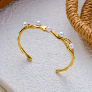 Detail van onregelmatige gedraaide gouden roestvrijstalen armband met parels