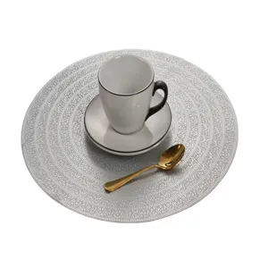 Nahaufnahme eines runden, silbernen PVC-Platzsets mit Kaffeetasse und goldenem Löffel.