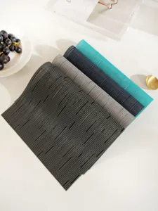 Detailed view of colorful woven PVC placemats stacked on a white table with lifestyle props.