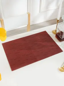 Detailed view of a dark red woven PVC placemat on a white dining table with chic props.