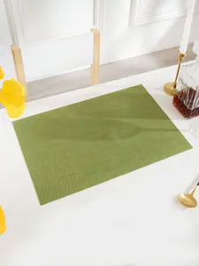 Close-up view of a stylish green woven PVC placemat on a neat white dining table setup.