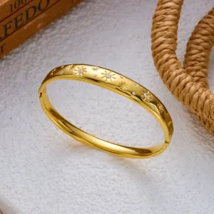 Detailopname van gouden roestvrijstalen armband met sterrengravure en kristallen.