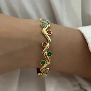 Detail van een vintage goudkleurige roestvrijstalen armband met gekleurde steentjes.