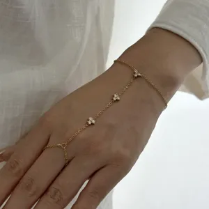 Gros plan d'une chaîne de main en acier doré avec des trèfles en zircon sur une main