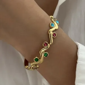 Close-up van gouden roestvrijstalen armband met veelkleurige stenen en gedraaid design