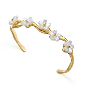 Eleganter goldener Armreif mit zarten weißen Blumenanhängern und goldenen Mitten