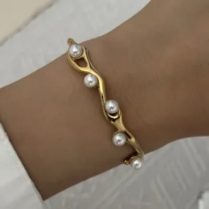 Elegante gouden golvende roestvrijstalen armband met kleine witte parels om de pols