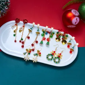 Set di orecchini natalizi festivi con campanella, albero e ghirlanda su piatto bianco.