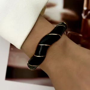 Detail view of a vintage black enamel bangle with twisted gold trim on a wrist.